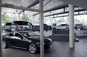 Innenraum eines Mercedes-Benz-Autohauses in Heiligenstadt. Im Vordergrund sieht man ein elegantes schwarzes Fahrzeug, im Hintergrund weitere ausgestellte Modelle auf verschiedenen Ebenen. Der Showroom wirkt modern, hell und großzügig, mit großen Fensterfronten und viel Tageslicht.