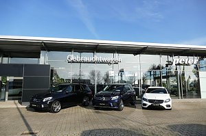 Glasfassade des Autohauses Peter mit der Aufschrift ‚Gebrauchtwagen‘. Davor stehen drei Mercedes-Modelle: zwei schwarze SUVs und ein weißer Kombi, alle mit dem Schild ‚Junge Sterne‘. Blauer Himmel, Spiegelungen von Bäumen und Umgebung in den Glasflächen.