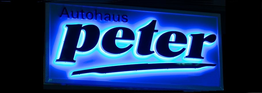 Leuchtendes Firmenschild mit der Aufschrift Autohaus Peter, Text mit blau leuchtendem Hintergrund.