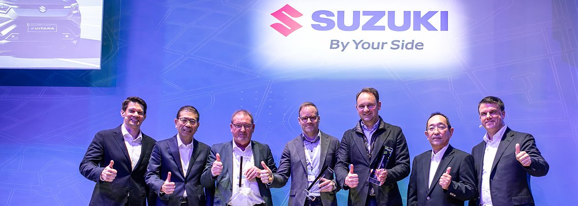 Mehrere Personen auf einer B&uuml;hne bei einer Preisverleihung, im Hintergrund das Suzuki Logo