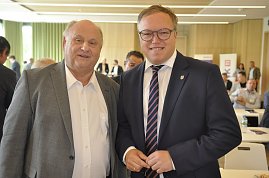 Das Bild zeigt links Geschäftsführer Helmut Peter und rechts Mario Voigt. Beide stehen nebeneinander in einem Konferenzraum, lächeln in die Kamera und tragen Anzüge. Im Hintergrund sind weitere Personen an Tischen zu sehen. (Foto: Michael Keller)