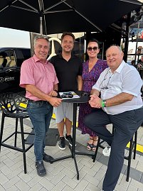 Gruppenfoto am Mercedes Cube: Centerleiter Marko Wuttke, Geschäftsführer Alexander Kästner, Geschäftsführerin Christina Dost und Seniorchef Helmut Peter stehen bzw. sitzen um einen Stehtisch unter einem Sonnenschirm. Auf dem Tisch liegen Prospekte und ein Modellauto. (Foto: Autohaus Peter)