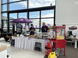 Verkaufsstand mit Snacks und Süßwaren im Autohaus Autowelt Peter. Unter einem lila Sonnenschirm stehen Verkäufer, daneben eine rote Popcornmaschine. (Foto: Autohaus Peter)