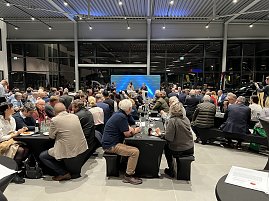 Frontale Ansicht der Bühne mit CDU-Hintergrund. Zwei Personen sprechen, während das Publikum an schwarzen Tischen zuhört. Der Raum ist hell beleuchtet und modern eingerichtet.