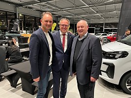 Andreas Peter, Mario Voigt und Helmut Peter stehen lächelnd nebeneinander in einem Autohaus. Im Hintergrund sind schwarze und weiße Fahrzeuge sowie weitere Gäste der CDU-Veranstaltung zu sehen.