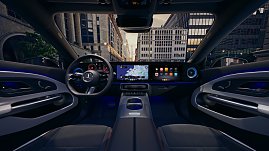 Das Bild zeigt einen weißen Mercedes-Benz CLA Shooting Brake, der auf einer breiten, nahezu leeren Stadtstraße fährt. Moderne Gebäude umgeben die Szene, das Licht wirkt weich und frühmorgendlich. Der Wagen ist seitlich zu sehen und vermittelt Dynamik sowie Eleganz.