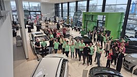 Gruppenfoto in einem Autohaus: Mitarbeitende und Gäste stehen zwischen mehreren Fahrzeugen und zeigen Daumen hoch.