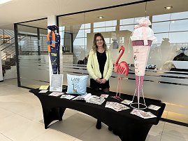 Frau steht hinter einem Infotisch mit Deko und Flyern, daneben große Schultüte und Flamingo-Figur im Autohaus.