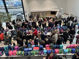 Viele Menschen in einem Autohaus, vor ihnen lange Tische voller bunter Schulranzen und Taschen.
