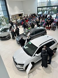 Blick von oben in ein Autohaus mit mehreren ausgestellten Skoda-Fahrzeugen und vielen Besuchern an Tischen mit bunten Schulranzen.