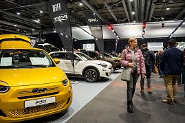 Gelber Fiat auf einer Automesse, flankiert von weiteren Fahrzeugen und Besucherinnen und Besuchern in einer gro&szlig;en Messehalle.