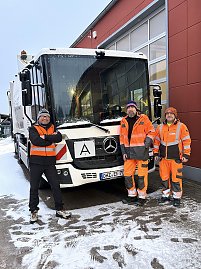 Zwei Mitarbeiter und unser Verkaufsberater Andr&eacute; Schmidt in orangefarbener Schutzkleidung stehen vor einem M&uuml;llfahrzeug im Schnee auf einem Betriebshof.