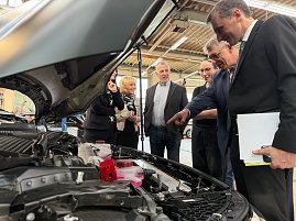 Teilnehmer des Pressegesprächs beim Rundgang in der Werkstatt an einem Fahrzeug bei offener Motorhaube.