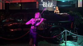 Close-up der Performance: Eine Violinistin spielt energiegeladen vor einem inszenierten Pickup, w&auml;hrend im Hintergrund eine DJane auflegt.