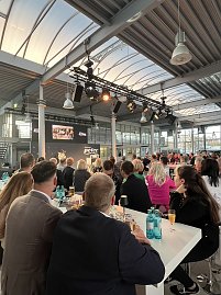 Die G&auml;ste schauen sich an Hochtischen einen Film an, der auf einer Leinwand abgespielt wird.