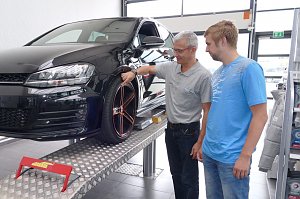 Mitarbeiter in der Werkstatt des �koda Autohauses erkl&auml;rt einem Kunden die Profiltiefe eines Reifens an einem schwarzen Auto auf der Hebeb&uuml;hne.