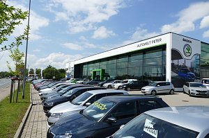 Gro&szlig;es �koda-Autohaus �Autowelt Peter� mit moderner Glasfassade und gr&uuml;nem Eingang. Davor stehen viele Neuwagen und Gebrauchtwagen in mehreren Reihen auf dem Parkplatz.