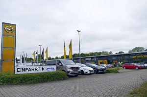Au&szlig;enansicht des Opel-Autohauses Peter in G&ouml;ttingen mit moderner Glasfassade, gelbem Opel-Logo, zahlreichen geparkten Autos und einem gro&szlig;en Einfahrt-Schild im Vordergrund.