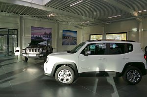 Heller Showroom mit einem weißen Jeep Renegade im Vordergrund und einem schwarzen Jeep Wrangler im Hintergrund, Poster mit Landschaftsmotiven an der Wand.