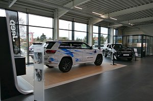 Showroom eines modernen Jeep-Autohauses mit großen Fensterfronten, zwei ausgestellte Jeep-Modelle, eines mit künstlerischer blauer Folierung, das andere in Schwarz.