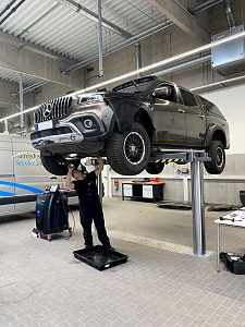 Mechaniker arbeitet unter einem angehobenen schwarzen Mercedes-Pick-up auf einer Hebeb&uuml;hne in der Werkstatt des Mercedes-Autohauses in Wittenberg.