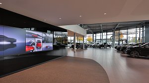 Moderner Ausstellungsraum eines Mercedes-Benz Autohauses mit gro&szlig;em LED-Bildschirm, vielen Neuwagen in heller, verglaster Halle.