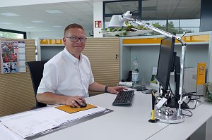 Ronny Peukert, Verkaufsberater, sitzt freundlich l&auml;chelnd an einem modernen Schreibtisch im hellen Autohaus-B&uuml;ro. Er tr&auml;gt ein wei&szlig;es Hemd und eine Brille. Auf dem Schreibtisch stehen ein Monitor, Tastatur, Maus, Schreibtischlampe und dekorative Elemente mit Opel-Logo. Im Hintergrund sind Schr&auml;nke und B&uuml;romaterialien zu sehen.