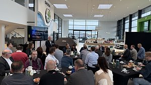 Ein Referent h&auml;lt einen Vortrag mit der Pr&auml;sentation Herausforderungen der Energiewende. Teilnehmende sitzen an runden Tischen mit Kaffee und Fr&uuml;hst&uuml;cksplatten.