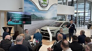 Ein Referent spricht vor einem Publikum, w&auml;hrend der neue �koda Elroq im Showroom pr&auml;sentiert wird. Links auf einem Bildschirm die Begr&uuml;&szlig;ungsfolie Herzlich Willkommen zum �KODA Unternehmerfr&uuml;hst&uuml;ck.