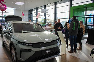Ein neues Škoda-Fahrzeug mit geöffnetem Kofferraum steht im hellen Showroom. Besucher unterhalten sich daneben, rosa Flamingo-Dekorationen hängen von der Decke.