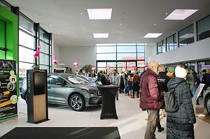 Großer Ausstellungsraum mit neuen Škoda-Fahrzeugen. Viele Menschen gehen durch die Halle. Rosa Flamingos sind als Dekoration aufgestellt.