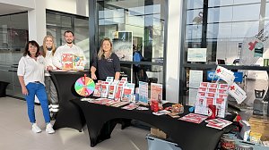 Vier Personen stehen hinter einem Infostand im Škoda Autohaus. Auf dem Tisch liegen Broschüren und ein Glücksrad. Die Personen tragen Kleidung mit Logos des Deutschen Roten Kreuzes.