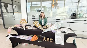Eine Frau sitzt hinter einem Stand im Autohaus. Auf den Tischen liegen farbenfrohe, große Schultüten und Informationsmaterialien. Vorne große Buchstaben ABC.