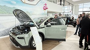 Ein helles Škoda-Fahrzeug mit geöffneter Motorhaube und Fahrertür steht im Showroom. Besucher betrachten das Auto, im Hintergrund Flamingo-Dekoration.