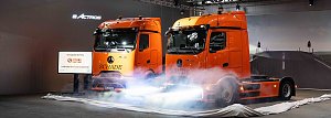 "Zwei orangefarbene Mercedes-Benz eActros-Lkw mit Schade-Logo während einer Fahrzeug-Enthüllung mit Nebeleffekten.