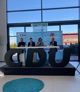 Frontalaufnahme der Podiumsdiskussion mit vier Personen, mittig Colette Boos-John. Vor ihnen gro&szlig;e CDU-Buchstaben, im Hintergrund Team Merz 2025-Plakat.