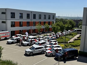 Gesamtansicht des DRK-Fuhrparks: Luftaufnahme des Innenhofs vor einem DRK-Gebäude mit zahlreichen Einsatzfahrzeugen, einem Rettungswagen und Mitarbeitenden, die neben den Autos stehen.