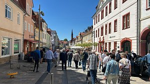 Fußgängerzone in Heiligenstadt voller Menschen bei strahlendem Sonnenschein. Rechts Cafés mit weißen Sonnenschirmen, links bunte Altstadthäuser.
