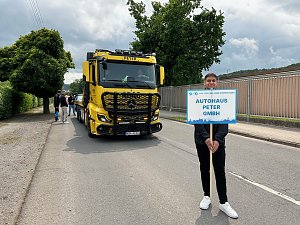 Ein junger Mann steht auf einer Stra&szlig;e und h&auml;lt ein Schild mit der Aufschrift Autohaus Peter GmbH bei einem Festumzug in Sondershausen anl&auml;sslich 900 Jahre Sondershausen. Hinter ihm steht ein gelber Mercedes-Benz Abschlepp-Lkw mit der Aufschrift Peter auf der Windschutzscheibe. Weitere Personen und Fahrzeuge sind im Hintergrund zu sehen.