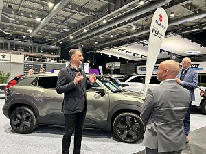 Andreas Peter erkl&auml;rt einen grauen SUV am Messestand, zwei Zuh&ouml;rer stehen davor. Im Hintergrund Suzuki-Banner und weitere Autos.