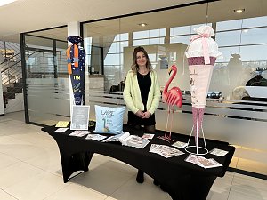 Frau steht hinter einem Infotisch mit Deko und Flyern, daneben gro&szlig;e Schult&uuml;te und Flamingo-Figur im Autohaus.