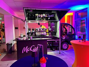 cCafé-Kaffeebar im Eventbereich mit buntem Licht und Stehtischen.