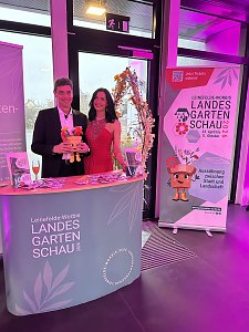 Zwei Personen am Messestand der Landesgartenschau mit Werbebanner und Flyern.