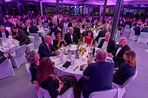 Gäste sitzen an gedeckten Tischen bei Gala-Event mit stimmungsvoller Beleuchtung.