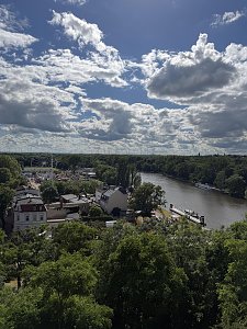 Blick auf die Saale und den Schausteller-Park. Der Himmel ist blau und mit Wolken durchzogen, im unteren Bild sieht man viele grüne Bäume.