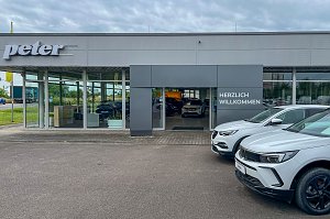 Der Eingangsbereich des Autohauses Peter in Halle Neustadt/ G&ouml;ttinger Bogen mit gro&szlig;er Glasfront und der Aufschrift "Herzlich Willkommen". Rechts vor dem Geb&auml;ude sind zwei wei&szlig;e Opel-Modelle zu sehen.