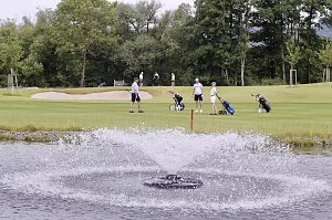 Golferinnen und Golfer bewegen sich mit Trolleys entlang des Fairways am Wasser.