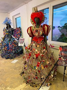 Zwei kunstvoll gestaltete Schaufensterpuppen, die in einem Innenraum aufwendige, volumin&ouml;se Kleider aus ungew&ouml;hnlichen Materialien pr&auml;sentieren, wobei das vordere Kleid von roten Herzen und floralen Elementen gepr&auml;gt ist.