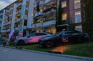 Zwei Mercedes-Benz Fahrzeuge, die nebeneinander auf einer beleuchteten Rasenfl&auml;che vor einer Wohnhausfassade pr&auml;sentiert werden.