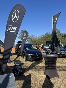 Stand vom Autohaus Peter. Im Vordergrund schwarze Mercedes-Fahnen, Sitzw&uuml;rfel und ein Stehtisch. Dahinter parkt ein EQT. Rechts daneben steht der neue elektrische GLC.